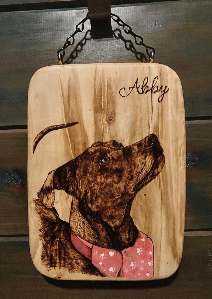 Image of a dog named Abby burned on a piece of wood.